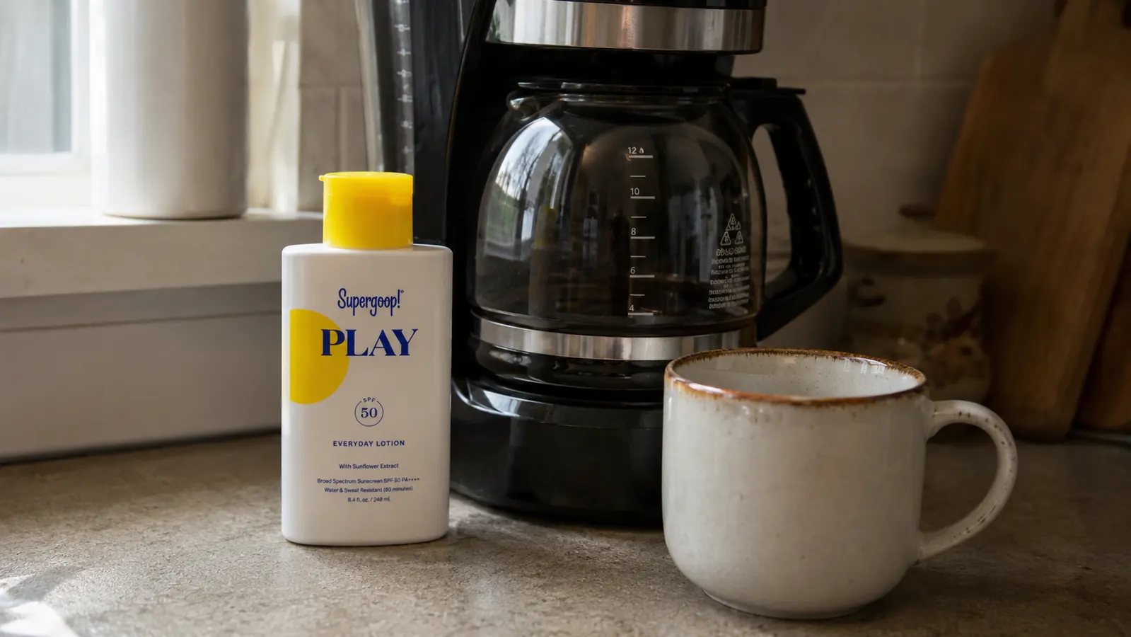 Sunscreen bottle sitting on a kitchen counter next to a coffee maker and a single mug