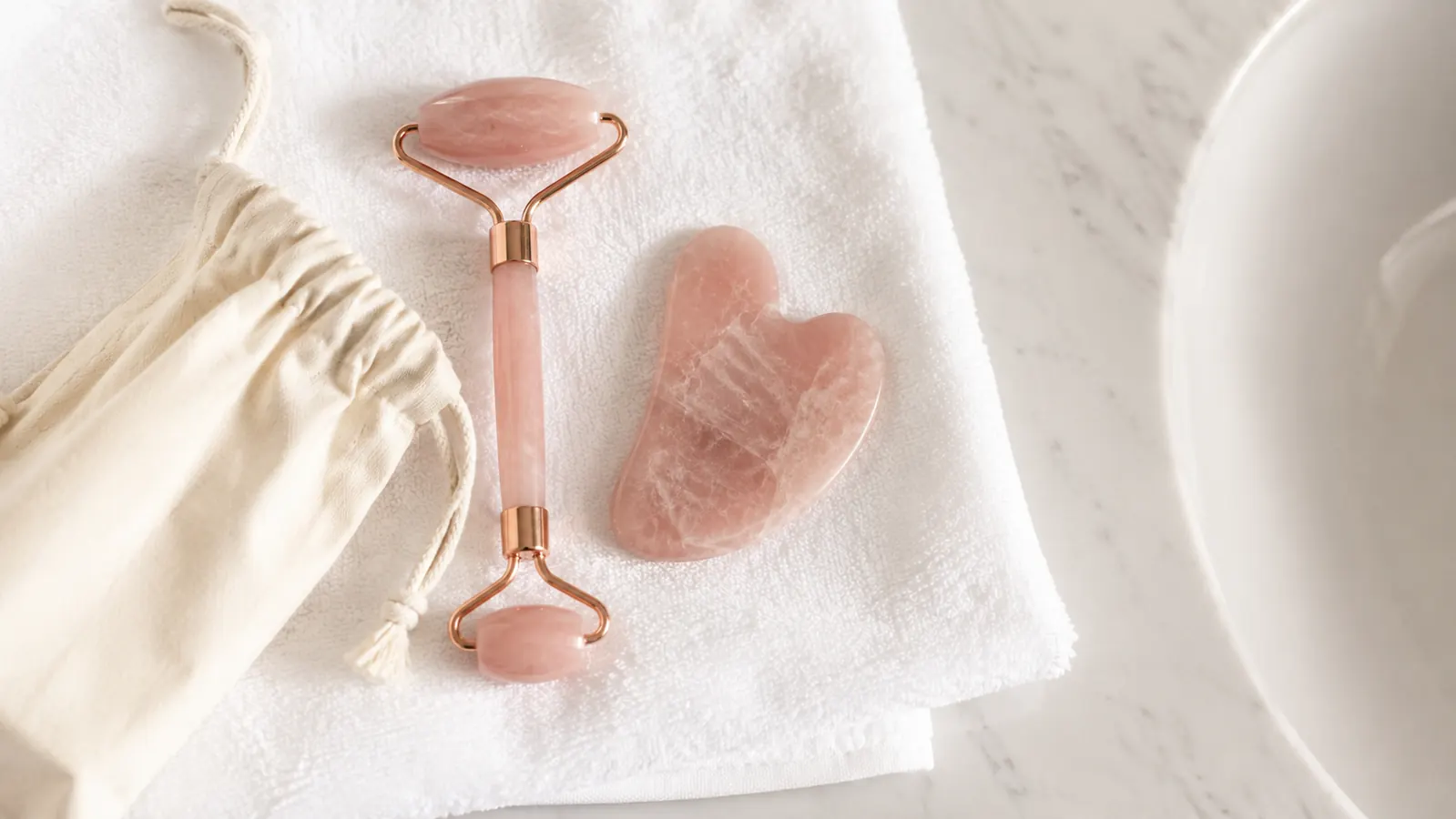 Rose quartz roller and gua sha stone drying on a folded towel next to a small storage pouch