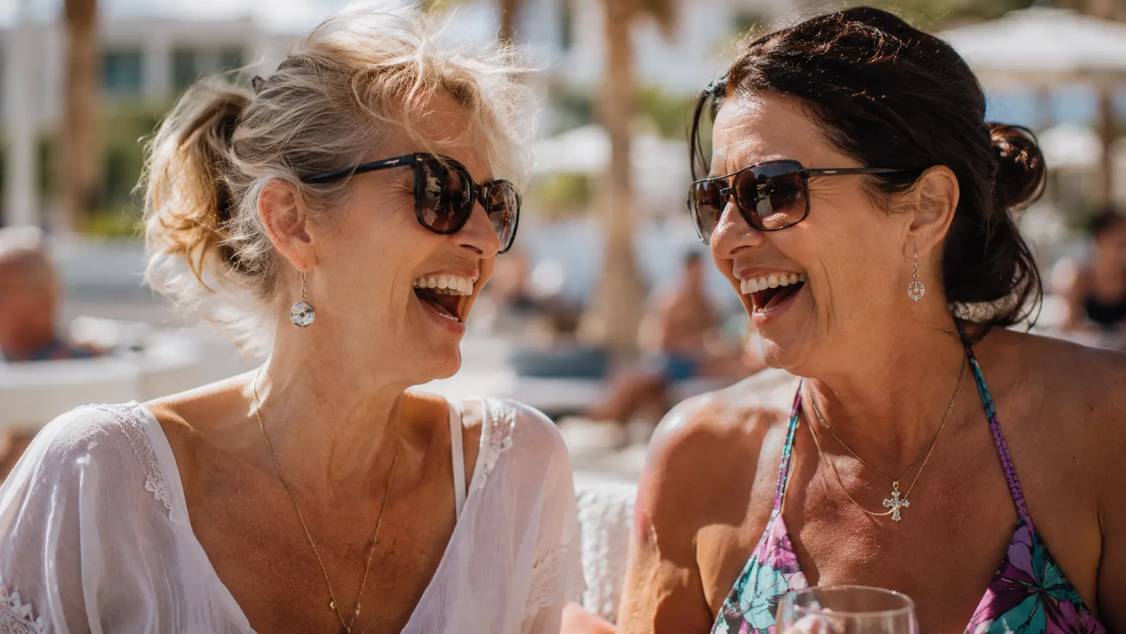 Two women laughing at an outdoor pool party, one wearing a scoop neck top with her neck fully visible