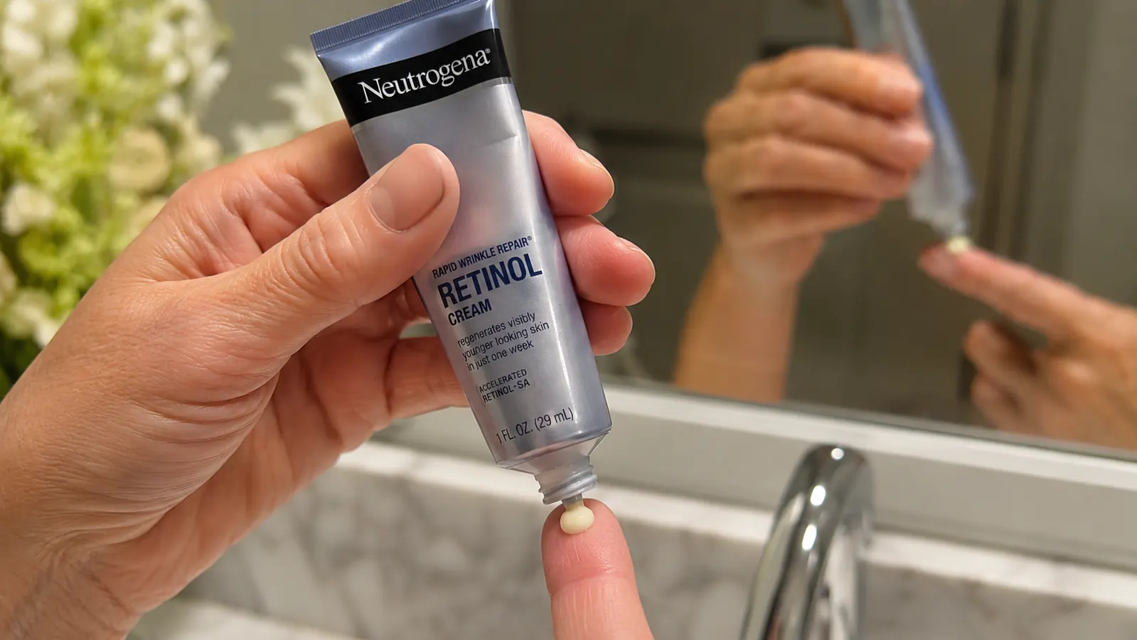 A hand dispensing a pea-sized amount of retinol cream onto a fingertip in front of a bathroom mirror