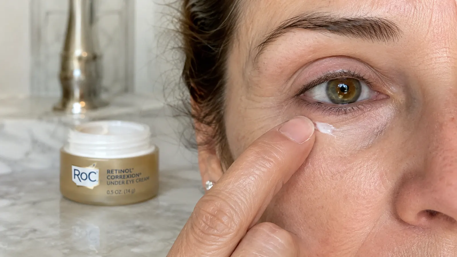 Hand applying a small dot of RoC Retinol Correxion Under Eye Cream with the ring finger below the lower lash line