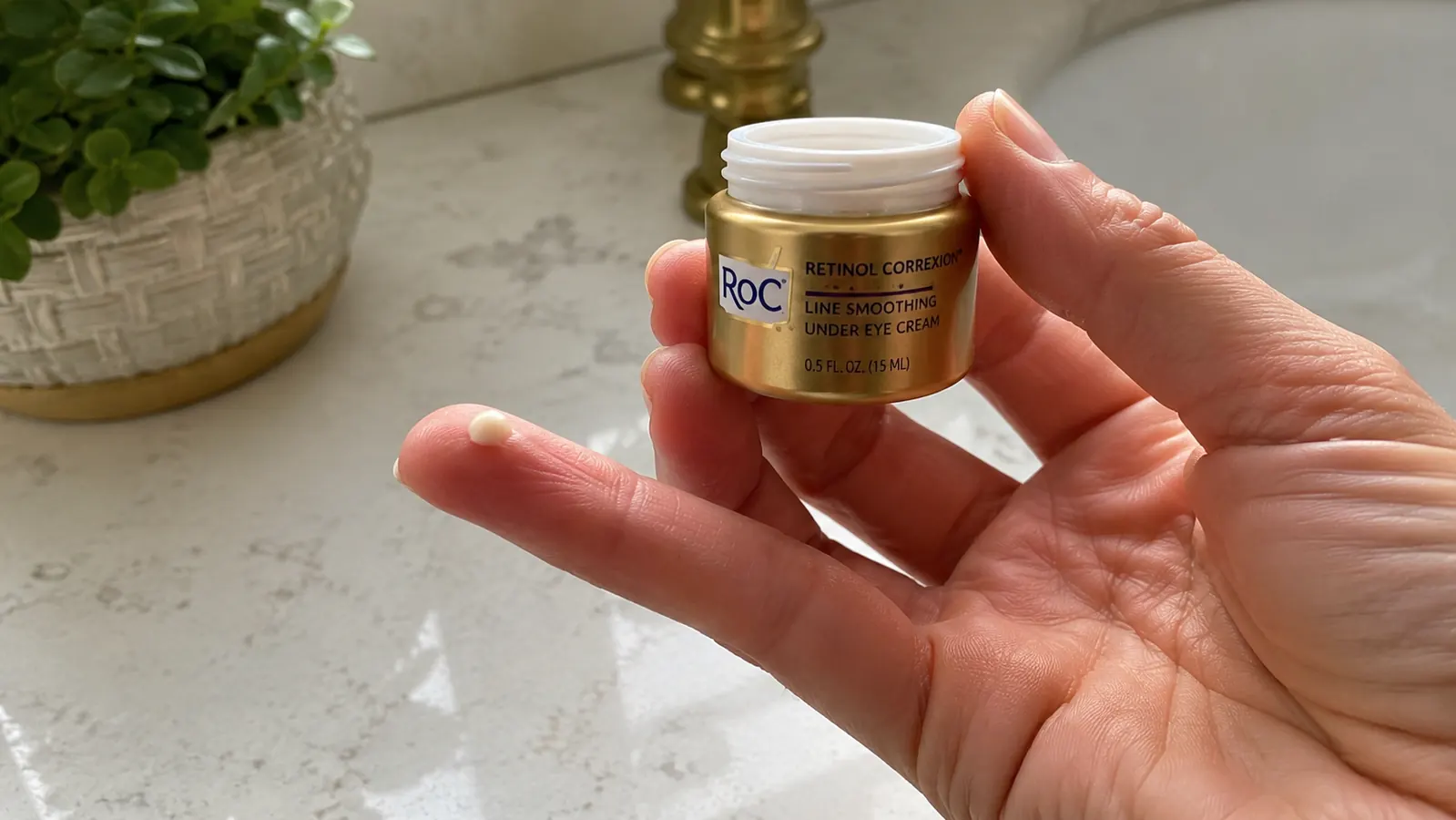 Hand dispensing a small rice grain amount of RoC Retinol Correxion Under Eye Cream from the jar onto a ring finger